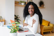 © Xavier Lorenzo - Young Latin American woman smile at camera working with laptop at home. Confident black female sitting on living room table using computer. Business and education concept