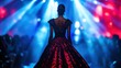 © ae - A model walks the runway in an elegant dress under dramatic lighting at a fashion show.