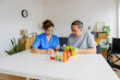 © Xavier Lorenzo - Female caregiver and senior man playing wooden shape puzzles game for dementia prevention