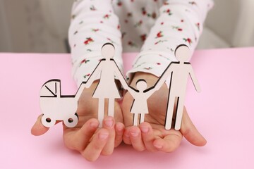 Wall Mural - Adoption. Little girl with figures of family at pink table, closeup