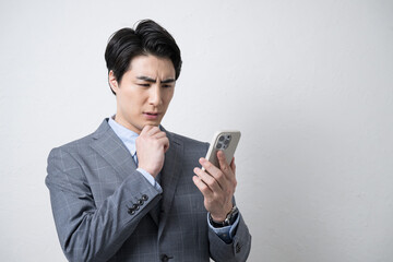 Businessman with smartphone (smart phone) in young suit, looking up with phone, troubled troubled thinking white background