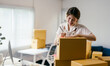 © PaeGAG - Young entrepreneur is writing an address on a cardboard box, managing her business from home. She is surrounded by packages, ready to ship