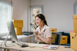 © PaeGAG - Asian small business owner celebrates success in her cozy office filled with boxes, paperwork, and a computer screen showing orders and inquiries