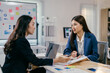 © PaeGAG - Two young businesswomen are having a serious conversation in a meeting, analyzing charts and data on a desk with a laptop