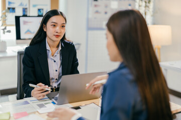 Fototapete - Two businesswomen having a discussion about work while sitting at a desk in an office. They are working together on a project