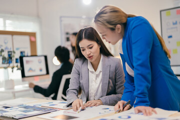 Two businesswomen in a modern office, deeply engaged in a productive meeting, discussing financial charts on a laptop, showcasing teamwork and collaboration