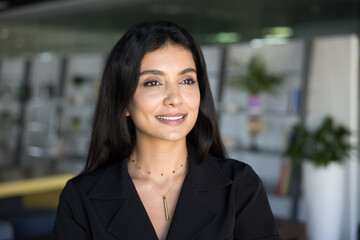 Happy thoughtful beautiful business leader woman posing in office co-working space, looking away with dreamy smile, thinking on career success, successful project, future startup, female leadership