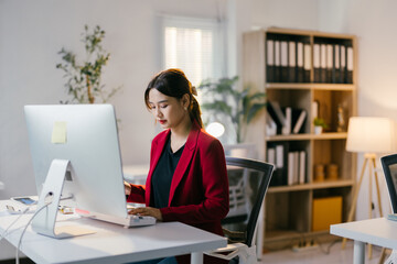 determined young businesswoman working at a modern office desk, typing on a computer. her red jacket