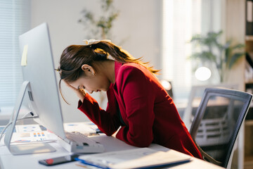 Stressed businesswoman with headache works on laptop in office, overwhelmed by job demands. Balancing work and mental health in tech-driven workplace