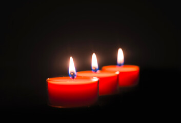 Wall Mural - Close-up of three burning candles on black background with copy space on top.