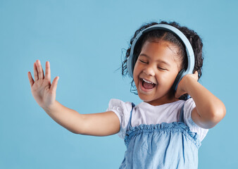 Studio, child and singing with headphones for dancing, hearing and happy with sound for audio track. Young female person, girl and listening with technology for music, radio song and blue background