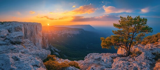 Wall Mural - majestic sunset over a rocky mountain range with a lone tree on the cliff edge.