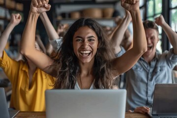 Diverse business team celebrating success in office with laptops and raised fists, cheerful and excited group in startup environment