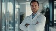 © Lion - Serious doctor in a white coat with crossed arms standing confidently in front of a bright office, looking at the camera, daylight