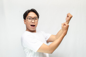 attractive young Asian man dancing hapily with a yes hand gesture and raising his fist to celebrate an achievment isolated over a white background. 