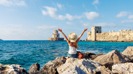 Young woman sitting on rock enjoying beautiful view of the sea and greek heritage