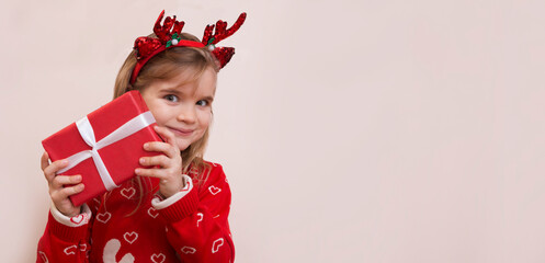 Portrait of a satisfied little child girl in a red sweater  laughing isolated over beige background. Holds Christmas gift boxes. Christmas time. copy space. banner