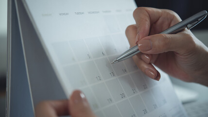 Closeup, woman hand writing on calendar event planner to set timetable organize schedule, event planning for business meeting or vacation plan. Organization and business planning concept.