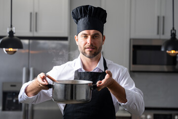 modern chef in professional uniform. close-up on the hand of male chef who is stirring soup in pot with spoon. cooking, culinary and people concept - male chef in toque with pot or saucepan.