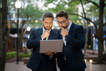 Two entrepreneurs near the office on the street. Business meeting of friends outdoors. Business mens with takeaway coffee and laptop outdoor. Business men team using laptop outdoor. Two businessman