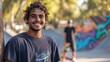 © Real People - A young Aboriginal man smiles confidently in a casual shirt at a vibrant outdoor skatepark, capturing the essence of youth culture and carefree energy in a lively atmosphere.