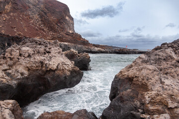 Ocean waves crashing on volcanic rocks on cloudy day