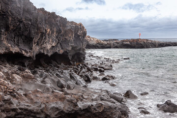 Ocean waves crashing on volcanic rocks on cloudy day