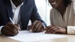 © Phongsri - A friendly young African realtor handing a couple pens to sign a real estate agreement, smiling confidently as they discuss the terms of their new home purchase