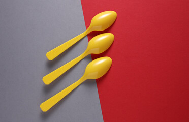 Yellow Plastic spoons on gray red background. Minimalism. Creative layout