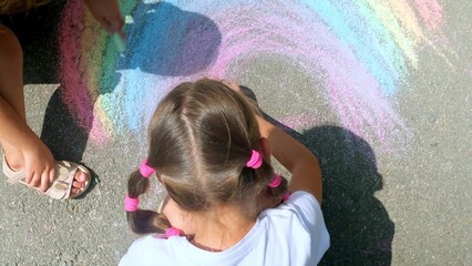 Kids paint outdoors. Children girl drawing a rainbow colored chalk on the asphalt on summer sunny day. Creative development of children