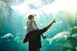 © C.Arcurs/peopleimages.com - Father, girl and back with fish in aquarium of education experience, marine learning and coral environment. Family, pointing and exhibit tank for sea creatures, biology and bonding together.