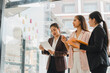 © kenchiro168 - Collaborative business meeting with three women discussing ideas and reviewing notes on glass board. They are engaged and focused on their project