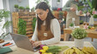 © Krakenimages.com - A woman florist using a laptop in a flower shop with a man arranging plants in the background.