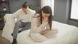 © Krakenimages.com - A concerned man watches a distraught woman sitting on a bed in a modern bedroom, embodying emotional support in a relationship.