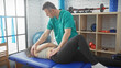 © Krakenimages.com - A physiotherapist man assists a woman patient in a rehab clinic room with equipment in the background.