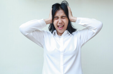 portrait of depressed asian young business woman screaming and shouting pushing her head with two palms, stressed with job deadline work pressure wearing white formal shirt, standing, mental health