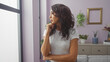 © Krakenimages.com - A contemplative middle-aged hispanic woman stands pensively in a modern living room interior.