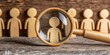 © Taskmanager - A wooden figure is under a magnifying glass, symbolizing attention, recruitment, evaluation, or scrutiny in a job or selection process.