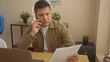© Krakenimages.com - Hispanic man engaged in a phone conversation while reviewing documents in a well-lit modern living room.