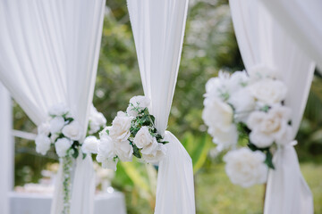 White flowers with green leaves tied together into a bouquet are attached to white cloth to decorate the wedding aisle, making it look beautiful and simple.