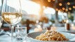 © Maximages  - A delicately plated pasta dish sits elegantly beside a glass of white wine on a softly lit restaurant table, creating a serene and inviting dining atmosphere.