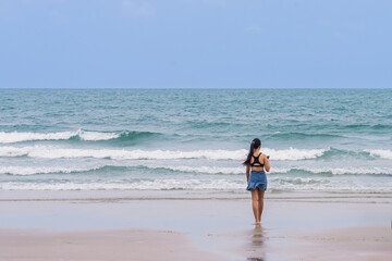 Back view of happy carefree woman using mobile phone at beach. Woman using smartphone standing at beach. Beautiful lovely young woman spending time at beach. Concept of travel, tourism and vacation.