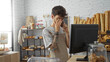 © Krakenimages.com - Young man with a beard looking stressed in a bakery while talking on the phone by a computer with bread and baked goods in the background