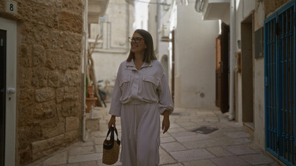 Wall Mural - A beautiful young hispanic woman is walking through the charming streets of polignano a mare, puglia, italy, enjoying the european atmosphere.