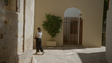 Wall Mural - Young hispanic woman walking through the town of lecce in puglia, italy, near historic buildings and archways.