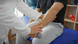© Krakenimages.com - A physiotherapist assisting a male patient with arm rehabilitation using a dumbbell in a clinic.