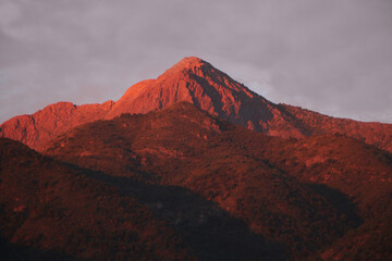 Majestic sunset over the mountain with sunlight shining in reddish tones contrast with the sky and clouds, natural panorama that evokes serenity and natural beauty