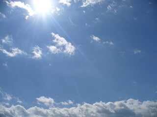 Optimistic, sunny blue sky with sun rays and white and grey clouds - natural background. Topics: weather, meteorology, sun energy, atmosphere, air space, season