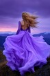 © Natalia - A woman in a flowing lavender dress stands on a mountain at sunset, her hair gently lifted by the breeze