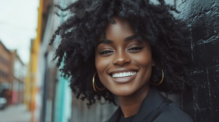 A joyful woman with natural curly hair leaning on a dark wall, exuding confidence and happiness, captures the essence of urban style and personal expression.